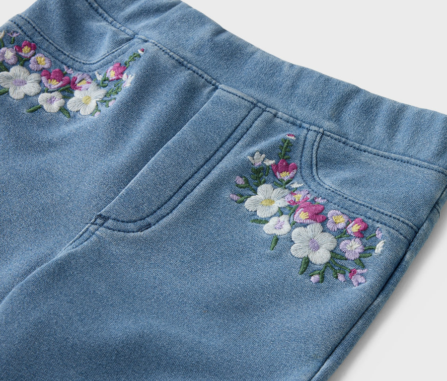 Nahaufnahme von hellblauen Jeans mit Blumenstickereien am Bund und an der Tasche.