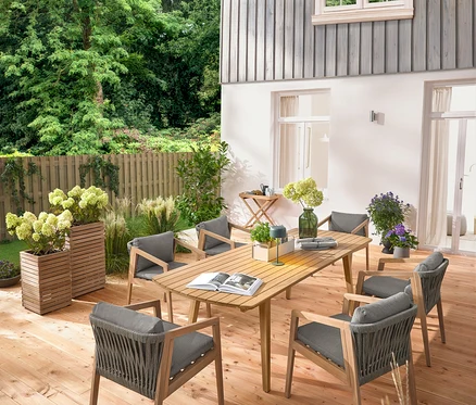 Auf einer Holzterrasse stehen ein ausziehbarer Gartentisch mit abgerundeten Fronten, ca. 180‒240 cm, sechs klassische Gartenstühle, ein Garten-Tabletttisch, eine Solar-Akku-Tischleuchte, dschungelgrün, und 2 Pflanzsäulen »Tinus«.