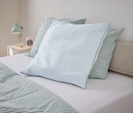 Ein hellblaues Kissen liegt auf einem Bett mit gestreifter Bettwäsche.
