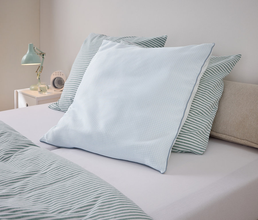 Ein hellblaues Kissen liegt auf einem Bett mit gestreifter Bettwäsche.