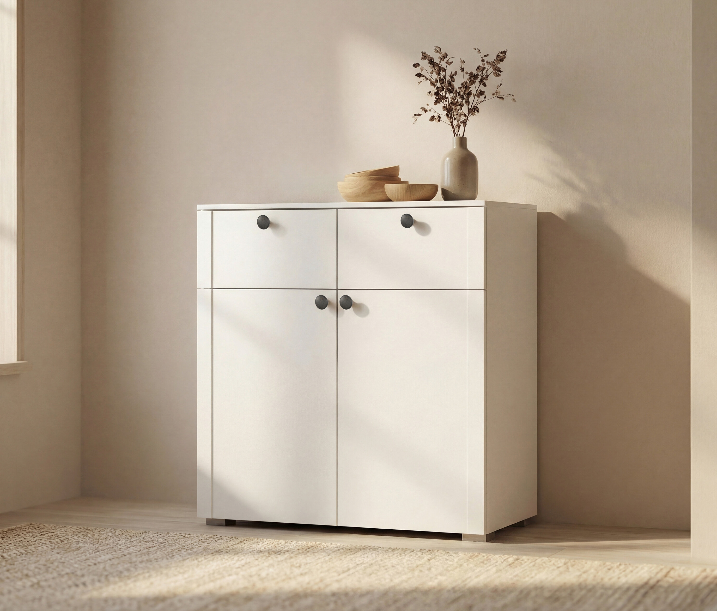 Weißer Schrank mit zwei Schubladen und zwei Türen. Auf dem Schrank stehen eine Vase mit Trockenblumen und drei Holzschalen.