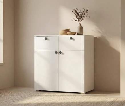 Weißer Schrank mit zwei Schubladen und zwei Türen. Auf dem Schrank stehen eine Vase mit Trockenblumen und drei Holzschalen.