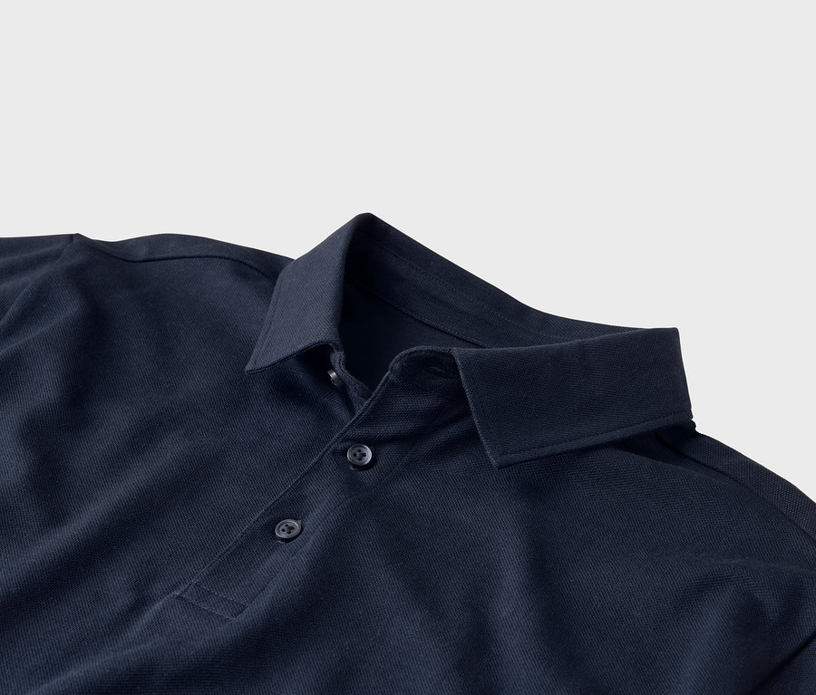 Nahaufnahme eines dunkelblauen Poloshirts mit Kragen und drei Knöpfen vor einem hellgrauen Hintergrund.
