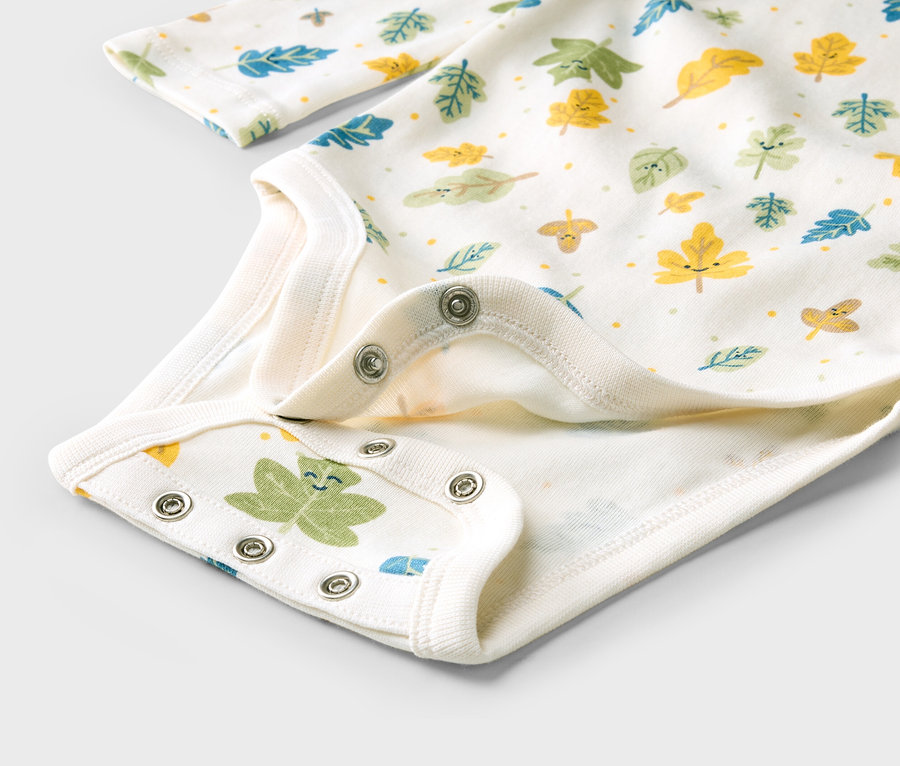 Nahaufnahme eines weißen Babybodys mit bunten Blättern und Druckknöpfen im Schritt.