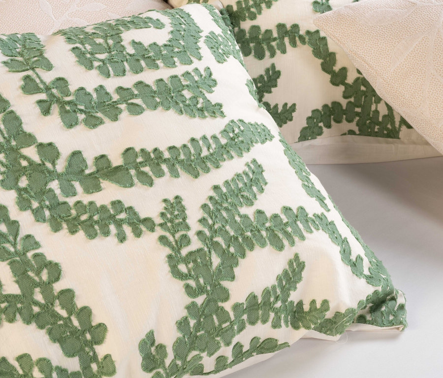 Nahaufnahme von zwei Kissen, eines mit grünem Farnmuster und eines mit cremefarbenem Muster.