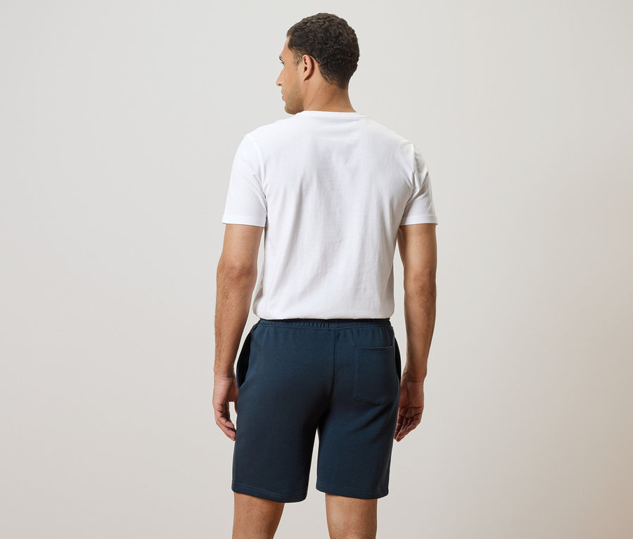 Rückansicht eines Mannes mit weißem T-Shirt und blauen Shorts.
