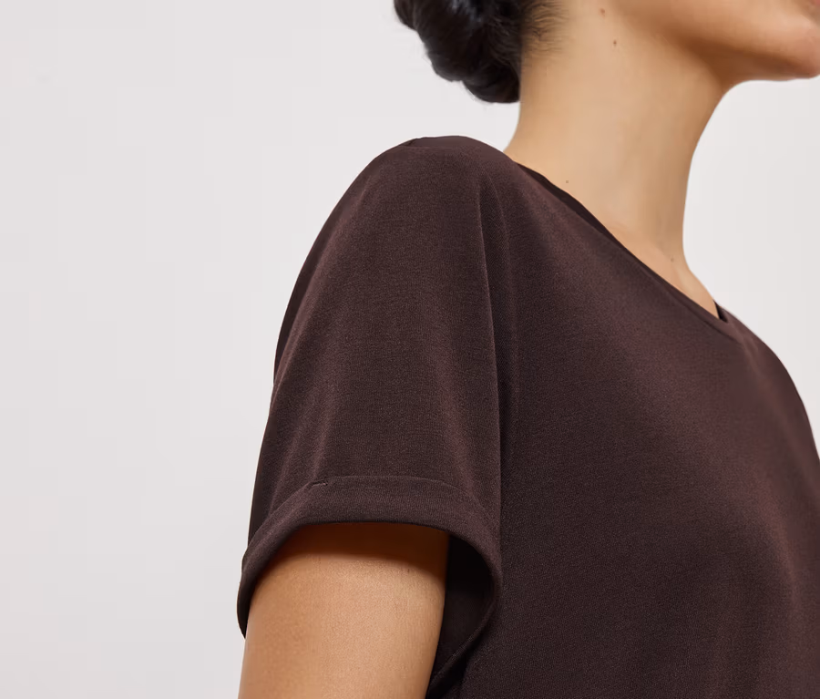 Nahaufnahme einer Frau mit hochgesteckten Haaren, die ein kastanienbraunes T-Shirt mit kurzen Ärmeln trägt.