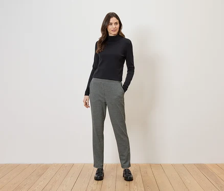 Frau mit schwarzem Rollkragentop und schwarz-weiß karierter Hose, die schwarze Slipper trägt.