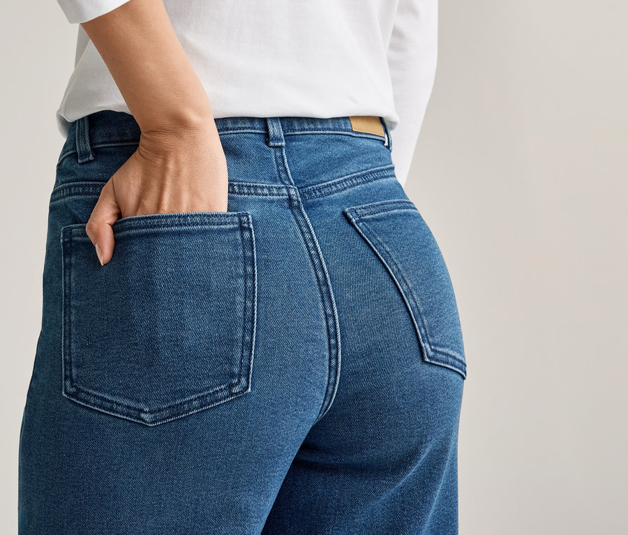 Frau mit Hand in der Gesäßtasche einer blauen Jeans, dazu ein weißes Oberteil.