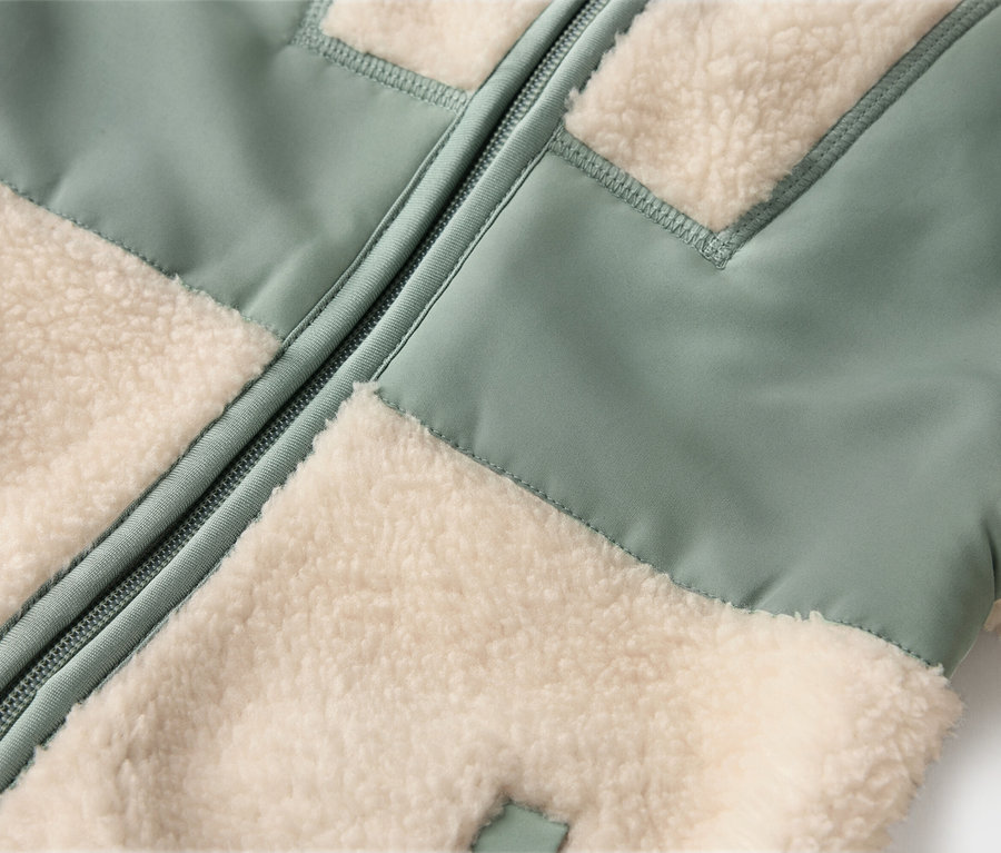 Nahaufnahme einer Jacke mit hellgrünen und cremefarbenen Fleece-Einsätzen und einem Reißverschluss in der Mitte.