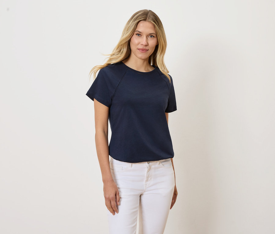 Blonde Frau trägt ein marineblaues T-Shirt und weiße Jeans.