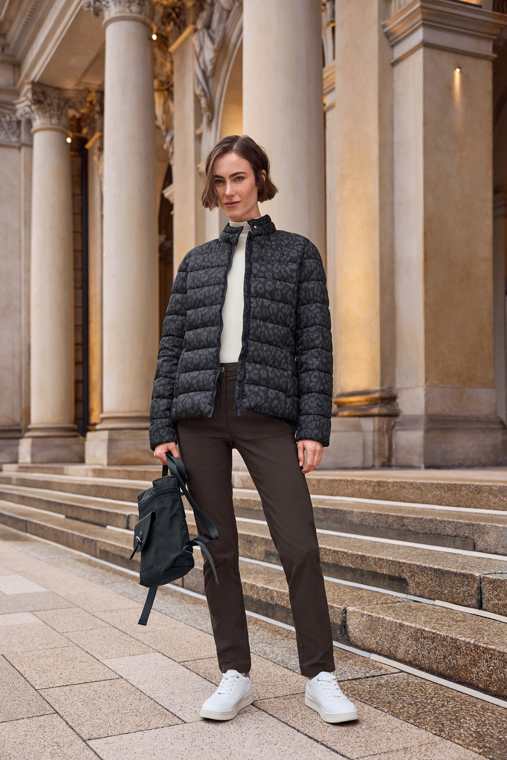 Frau steht vor einer Treppe, trägt eine Daunenjacke mit Leopardenmuster, braune Hose und weiße Tom Tailor Sneaker aus PU.