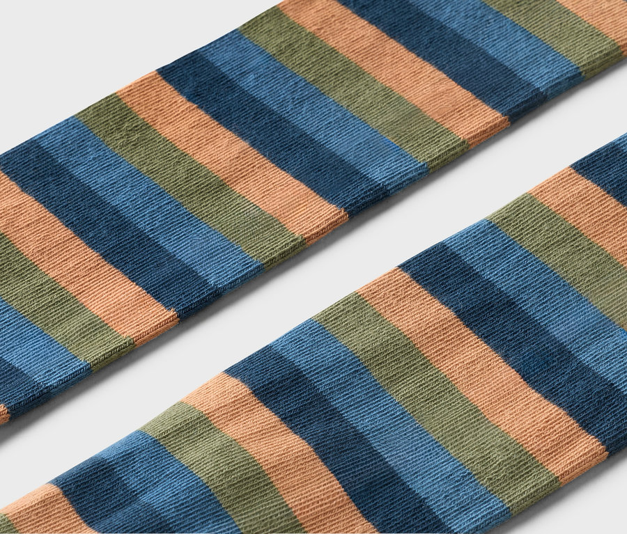 Nahaufnahme von zwei gestreiften Socken in Orange, Blau und Grün auf grauem Hintergrund.