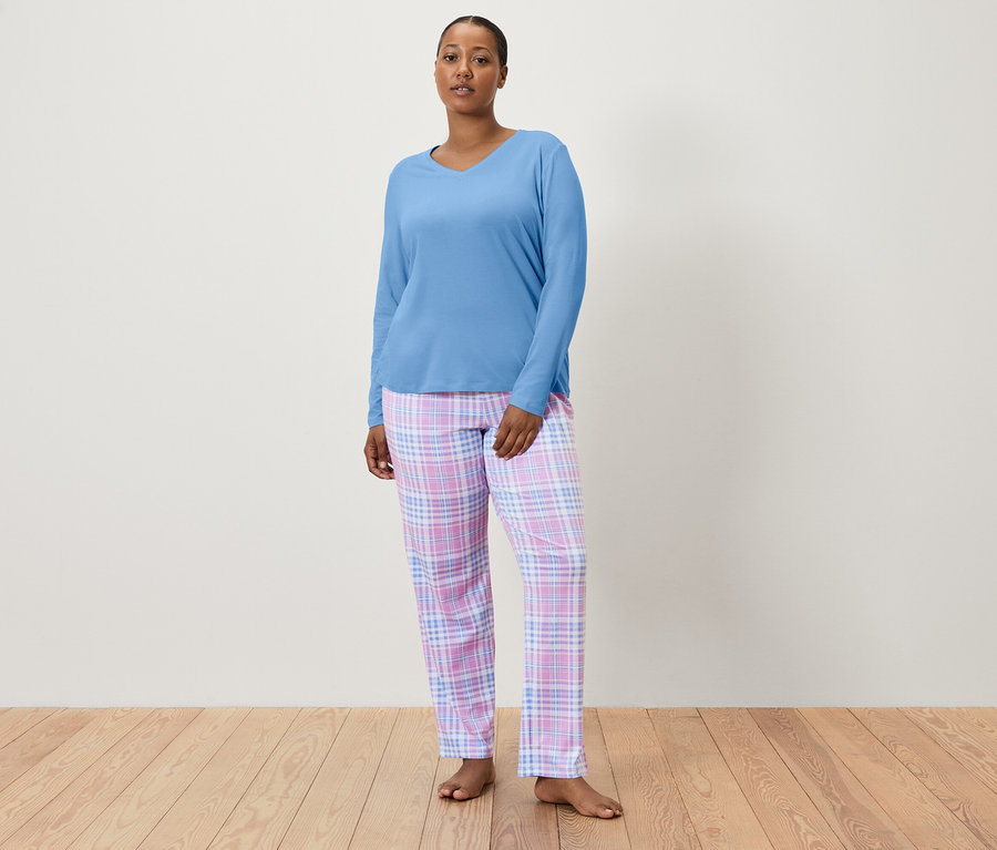 Frau trägt einen blauen Pyjamaoberteil und eine karierte Pyjamahose.