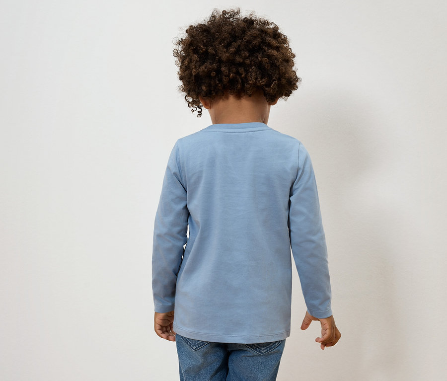 Rückansicht eines Kindes mit lockigem Haar, das ein hellblaues langärmliges Oberteil und Jeans trägt.