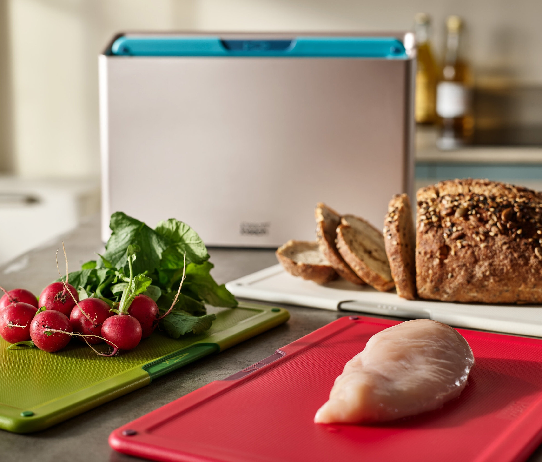 Radieschen auf einem grünen Schneidebrett, Hühnchen auf einem roten Brett und Brot auf einem weißen Brett.