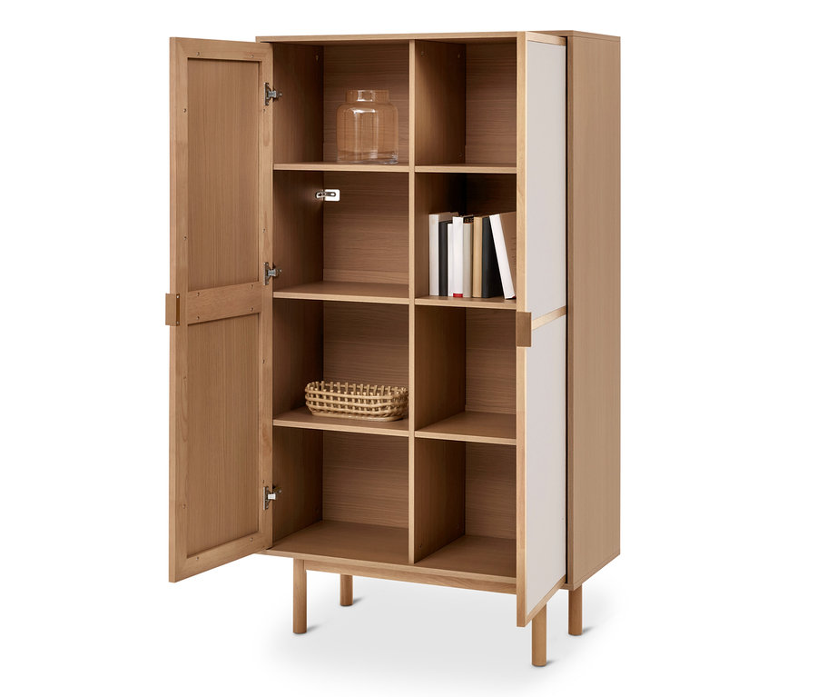 Heller Holzschrank mit offener Tür links, die Regale zeigt. Darin sind ein Glasgefäß, Bücher und ein geflochtener Korb sichtbar. Die rechte Seite hat weiße Paneele.