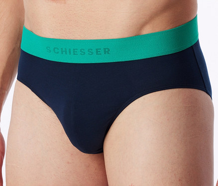 Nahaufnahme eines Mannes, der marineblaue Slips mit einem grünen Bund trägt, auf dem „SCHIESSER“ steht.