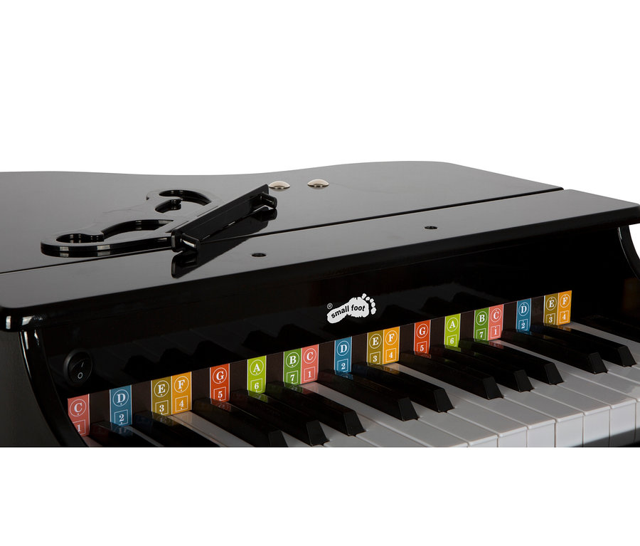 Ein glänzendes schwarzes Spielzeugklavier mit Notenständer. Seine weißen und schwarzen Tasten haben bunte Etiketten mit Buchstaben A-G und Zahlen 1-7. Das „small foot“-Logo ist sichtbar.