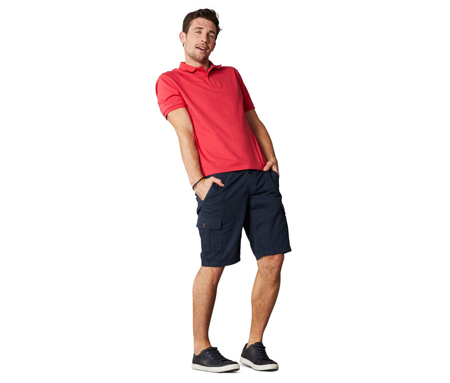 Mann posiert in rotem Poloshirt und Cargo-Shorts.