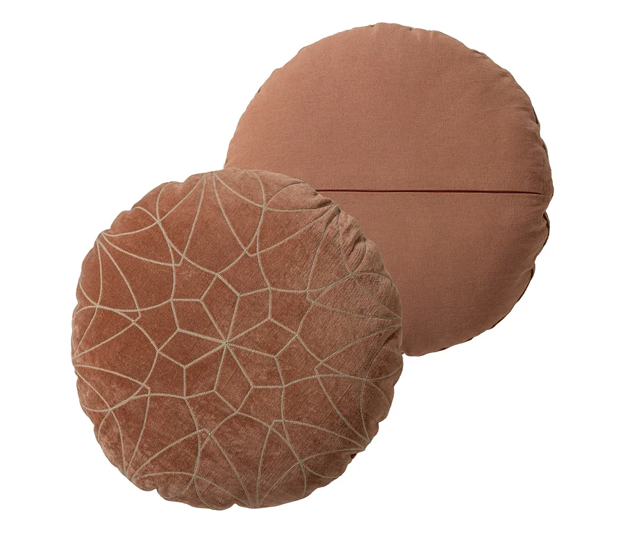 Zwei runde, terrakottafarbene Kissen. Das vordere Kissen ist kleiner, aus Samt und hat ein gesticktes geometrisches Muster. Das größere Kissen dahinter ist schlicht, aus Webstoff und hat eine horizontale Naht.
