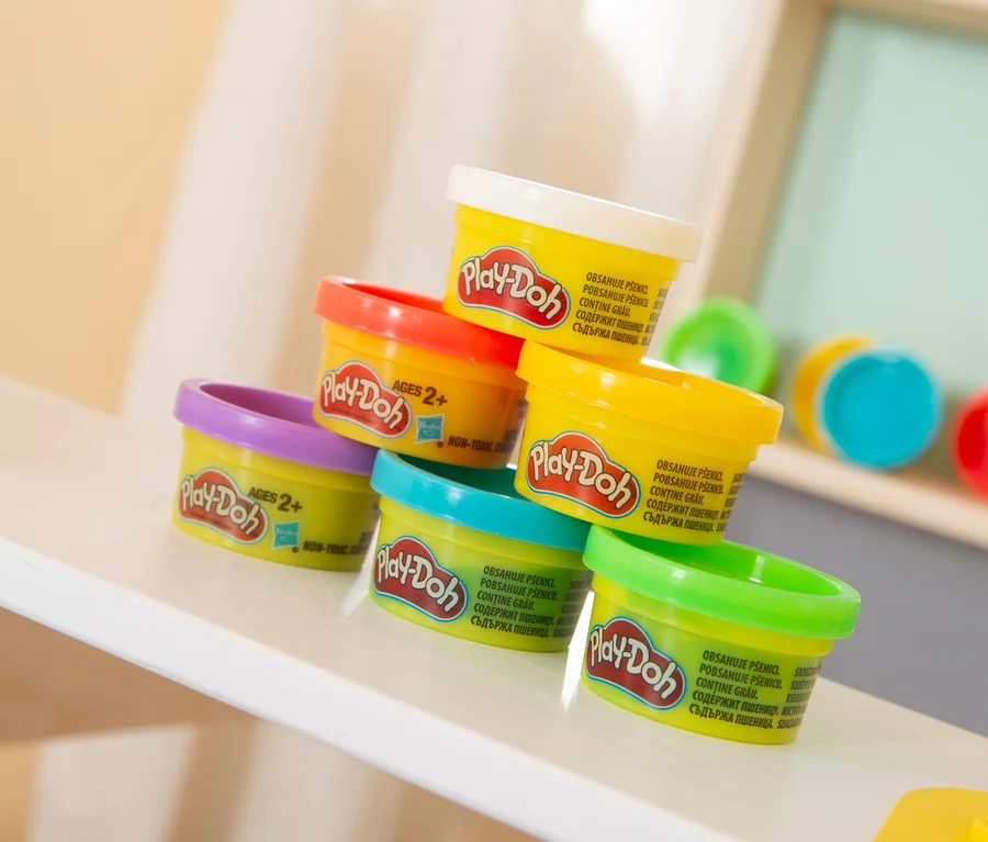 Ein Stapel aus sieben bunten Play-Doh-Dosen steht auf einem Regal.