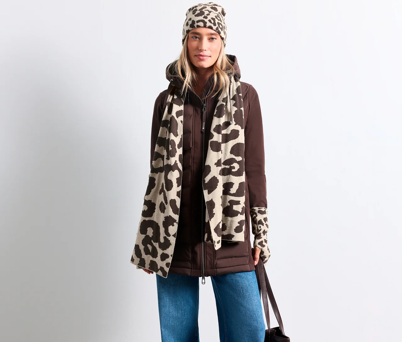 Frau in brauner Jacke, blauen Jeans, beigefarbenem Street One Feinstrickschal mit Leopardenmuster, passender Mütze und fingerlosen Handschuhen.