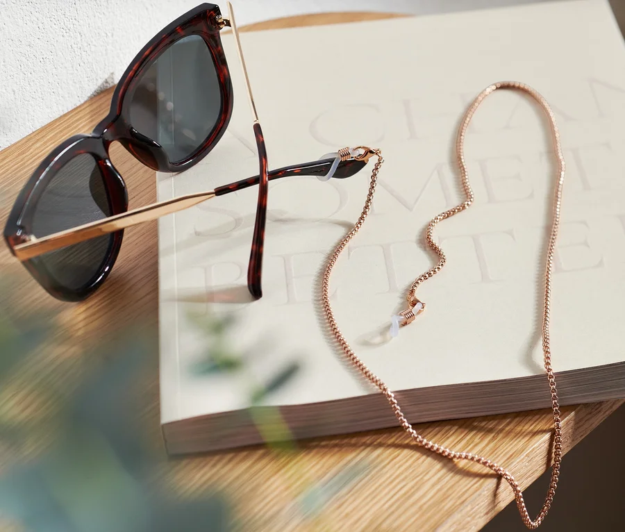 Sonnenbrille und Brillenkette liegen auf einem Buch auf einem Holztisch.