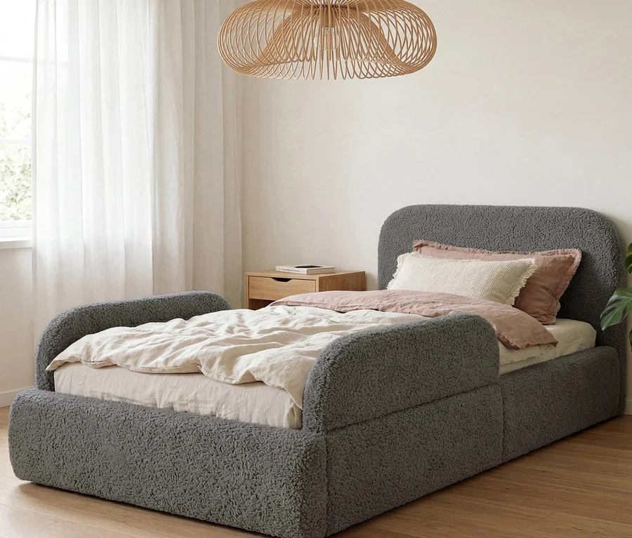 Graues Teddy-Stoffbett mit Kopfteil und Seitengittern, hellbeiger Bettwäsche, Holznachttisch und Holz-Pendelleuchte in einem Schlafzimmer.