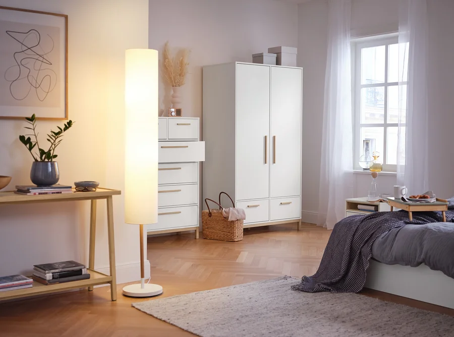 Im Schlafzimmer stehen ein Konsolentisch mit 2 Ablagen, eine Stehleuchte mit Textilschirm, ein Highboard »Eklund« mit Schubladen und ein Kleiderschrank »Eklund« mit Schubladen.