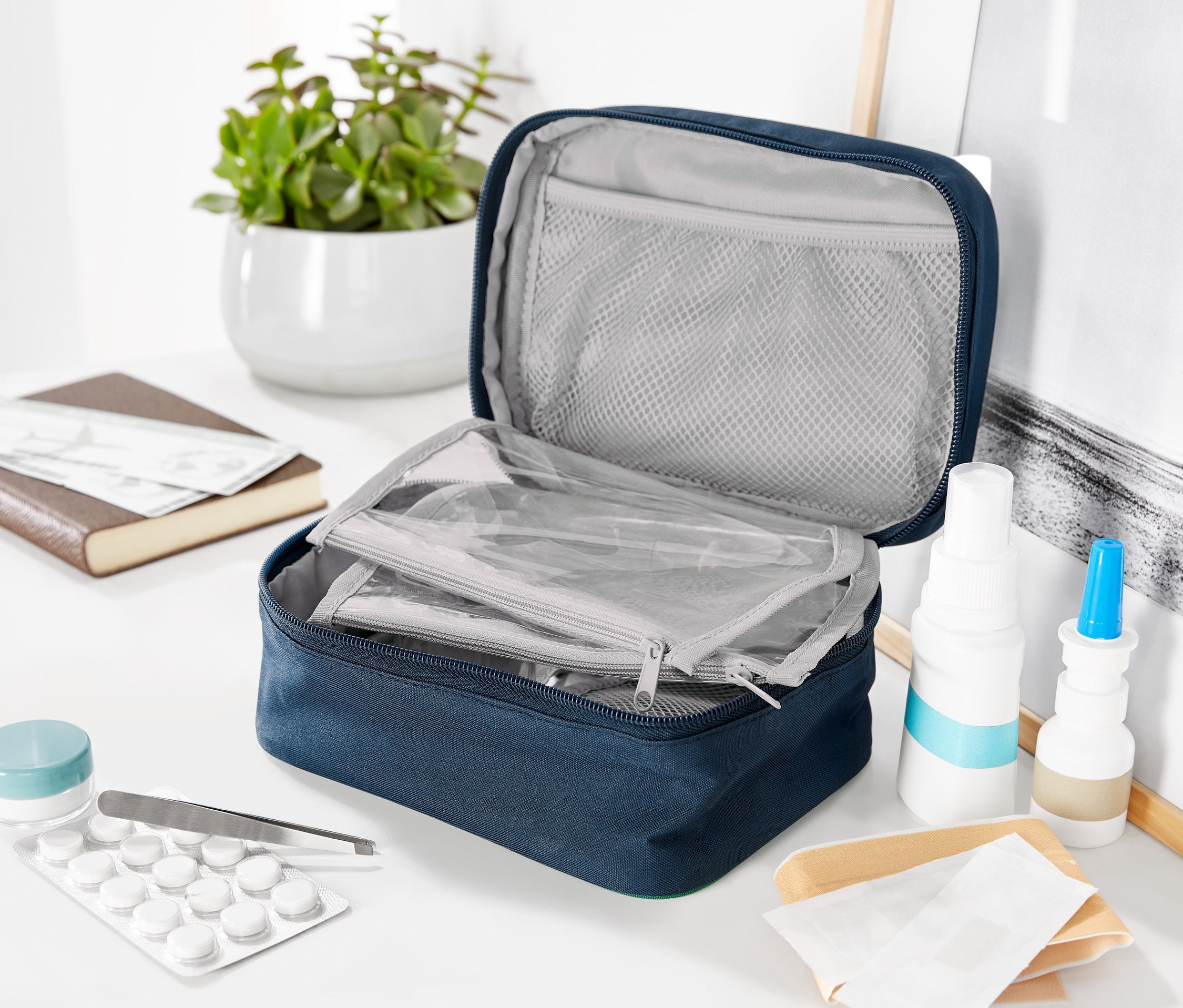 Geöffnete blaue Medikamententasche mit Netzinnentasche, Medikamente und Pflanze im Hintergrund.