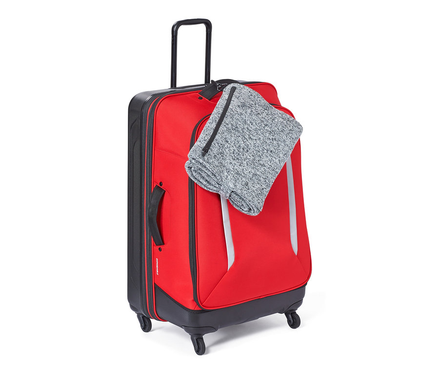 Roter Koffer mit Reisedecke oben drauf.