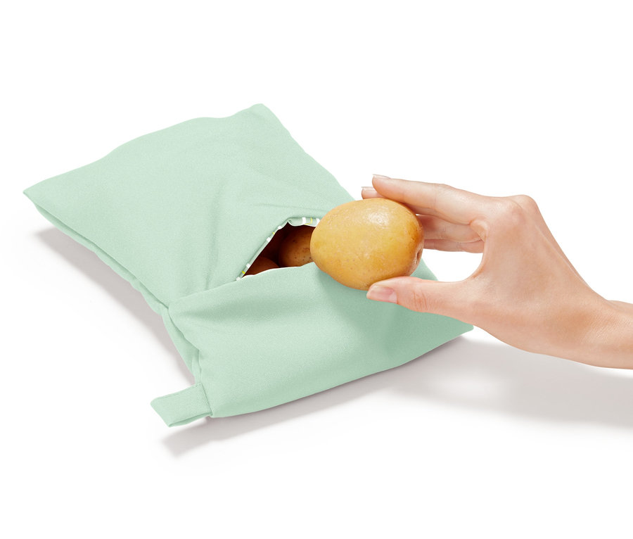 Eine Hand legt eine Kartoffel in eine hellgrüne Mikrowellen-Kartoffelgartasche.
