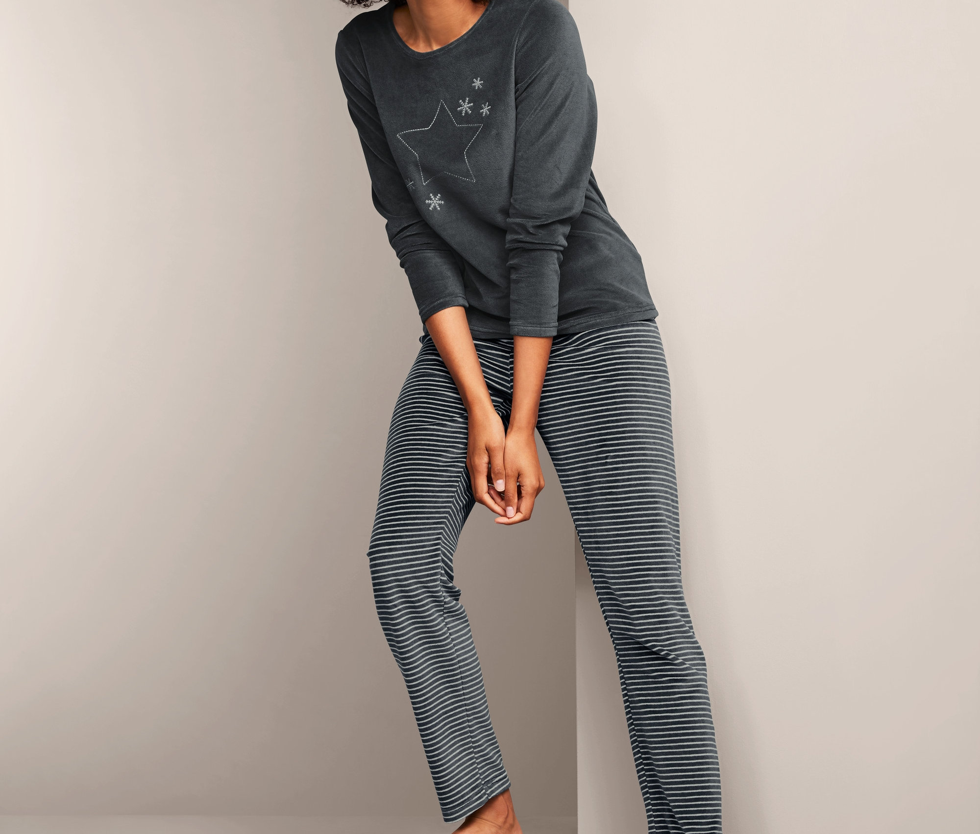 Frau posiert in Nicki-Pyjama mit Langarmshirt und gestreifter Hose.