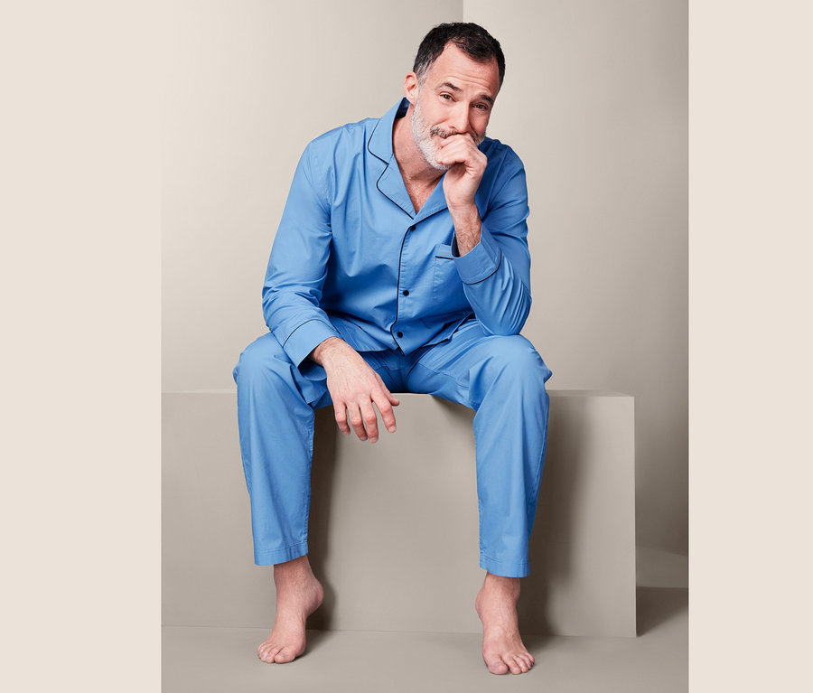 Mann sitzt mit der Hand am Kinn und trägt einen blauen Web-Pyjama.