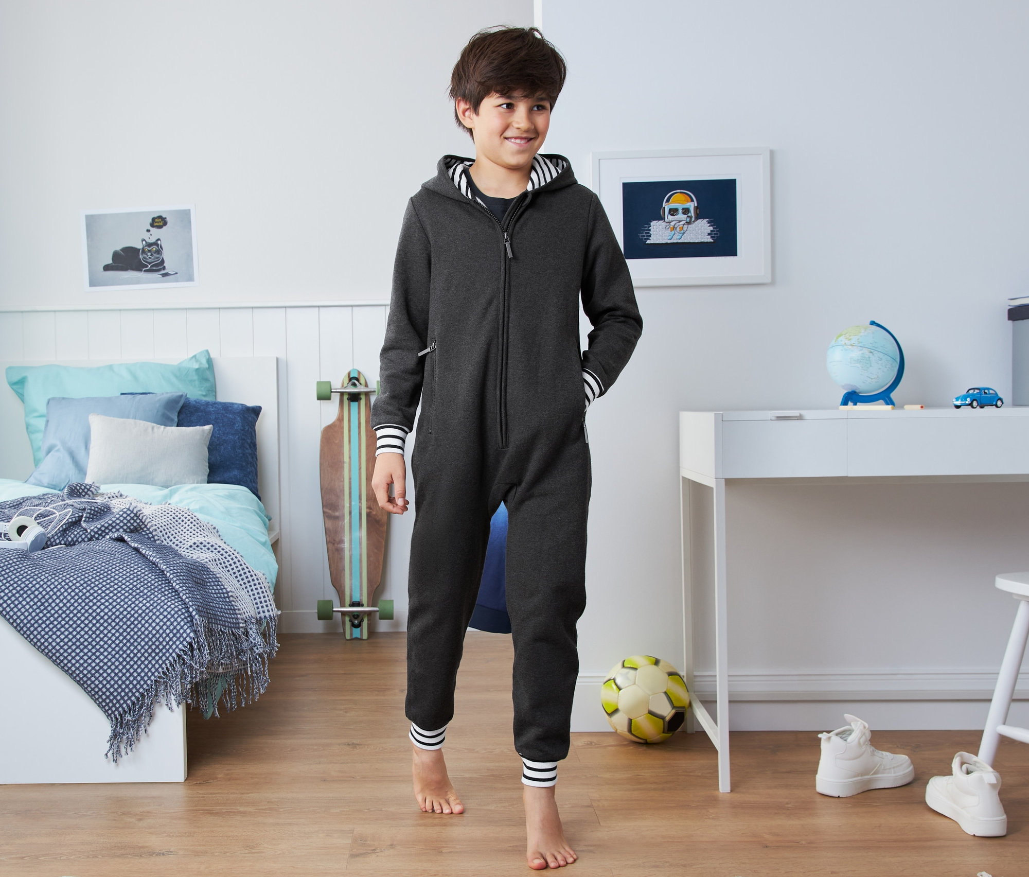 Junge im Kinder-Loungeoverall steht im Schlafzimmer.