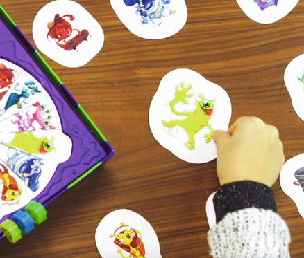 Kinderhand spielt Ravensburger »Monsterstarker Glibberklatsch« mit Monsterkarten auf einem Holztisch.