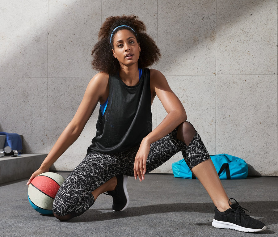 Frau mit Stirnband und schwarzem Sporttop kniet neben einem Basketball.