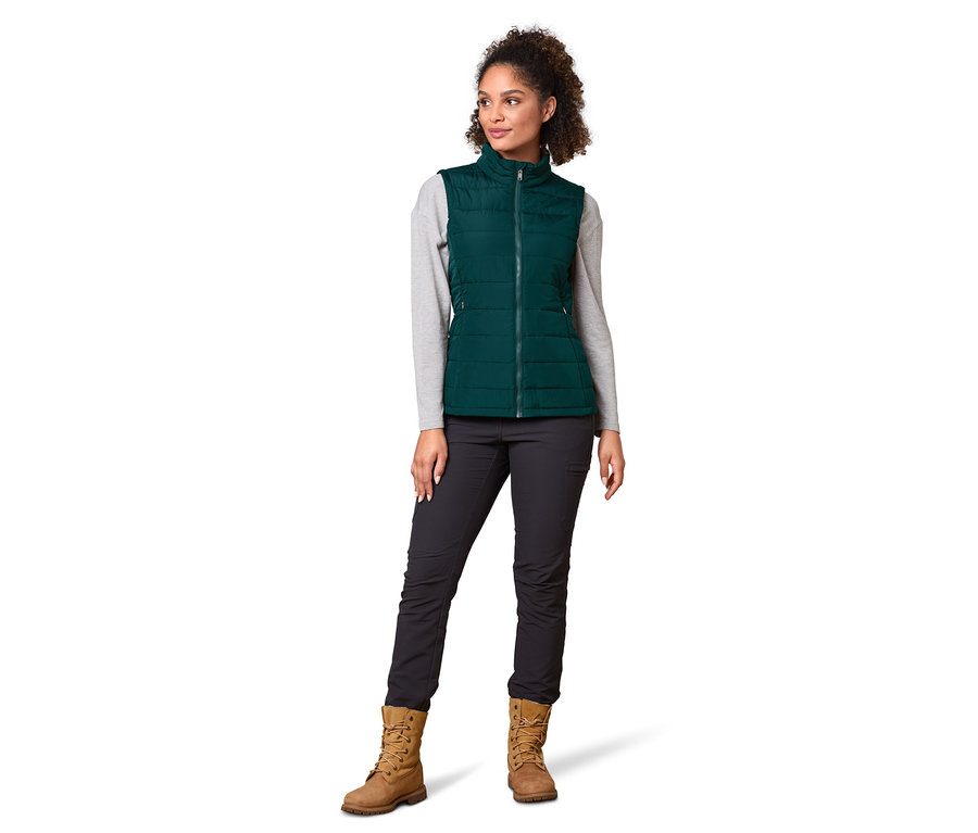 Frau trägt eine grüne Regenmantel mit Weste, ein graues Langarmshirt, eine schwarze Hose und braune Stiefel.