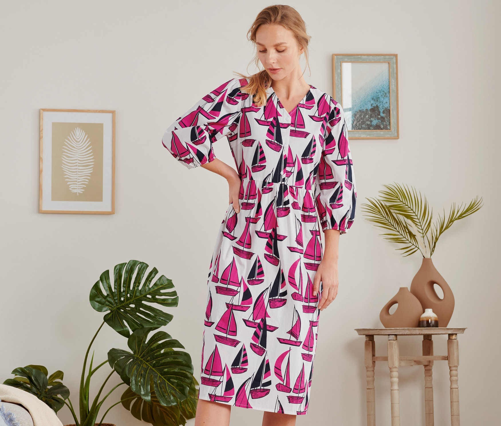 Frau steht im Raum und trägt ein Midikleid mit Segelboot-Print.