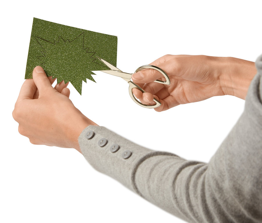 Person schneidet mit einem Bastelscheren-Set grünes Glitzerpapier.