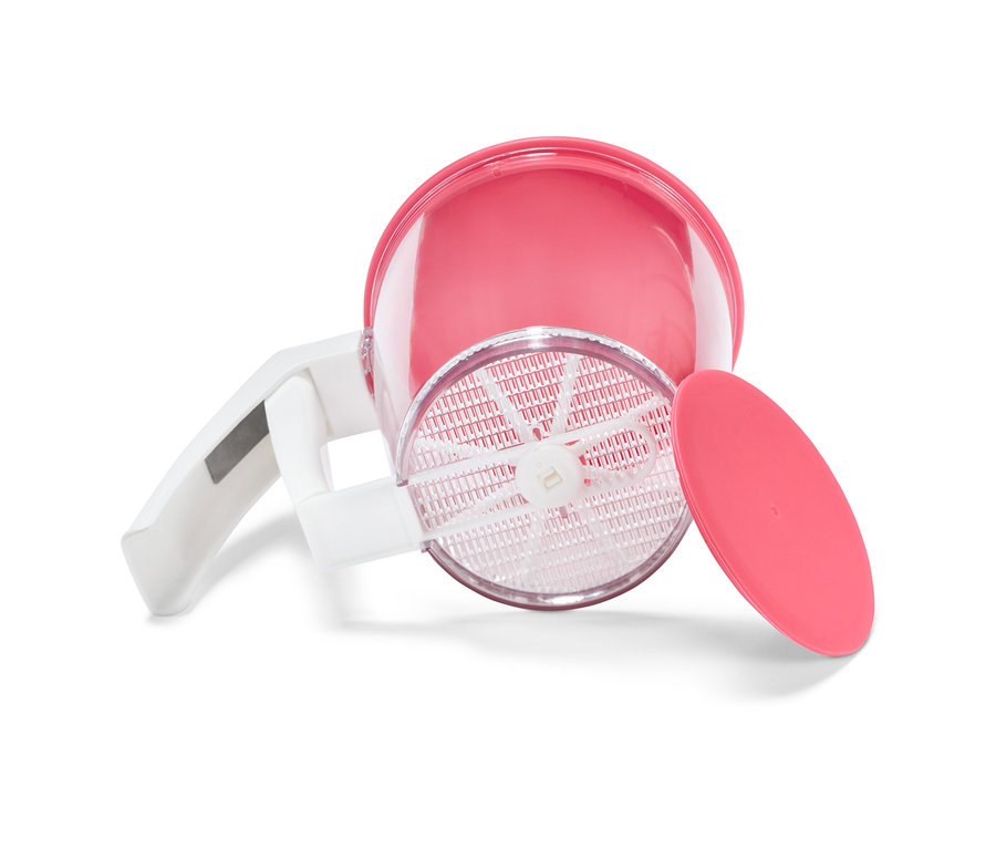 Ein pinkfarbenes Einhandsieb liegt auf der Seite, wobei der Deckel neben dem Sieb liegt.