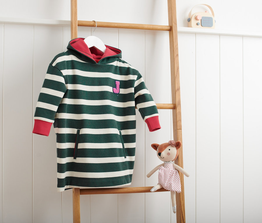 Gestreifter Longsweater mit Kapuze hängt an einer Holzleiter neben einem Spielzeug.