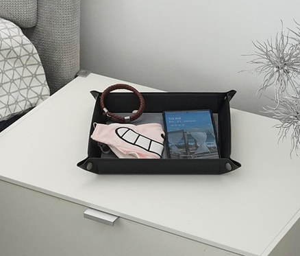 Nachttisch mit Taschenleerer mit Wireless Charger, Armband, Etui und Buch. Vase mit dekorativen silbernen Zweigen steht daneben.