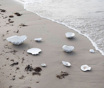 Am Strand liegen weiße Teller und Schalen in Muschelform.