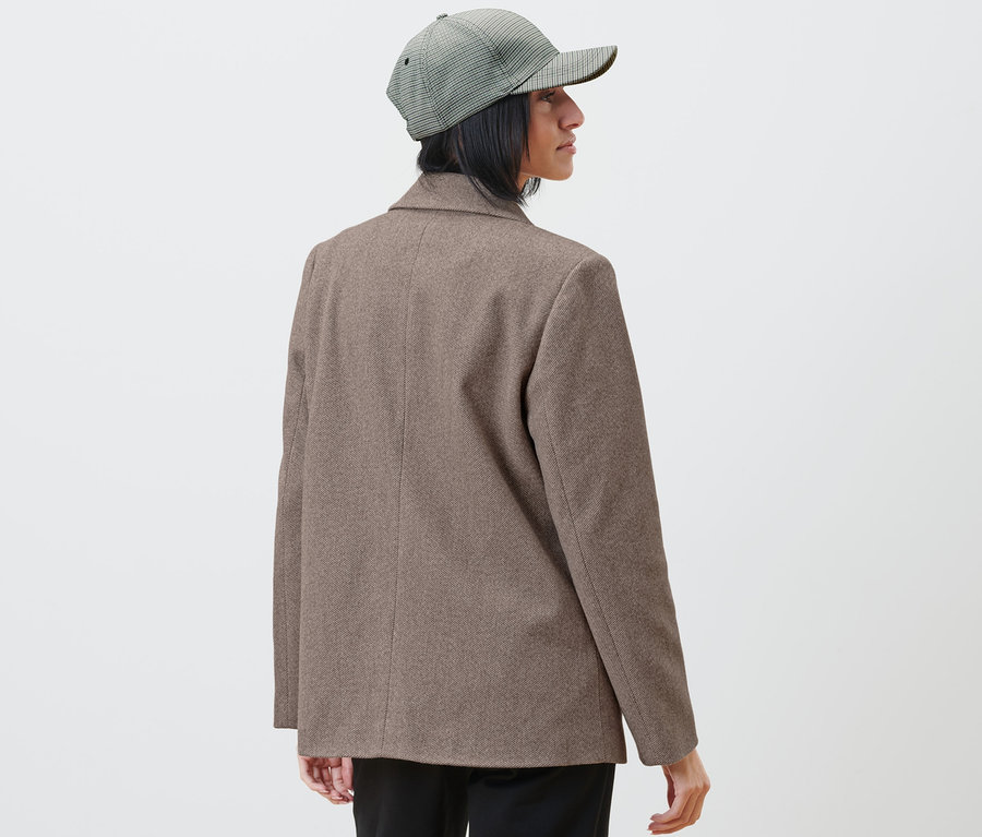 Frau mit Blazer und karierter Kappe schaut nach rechts.