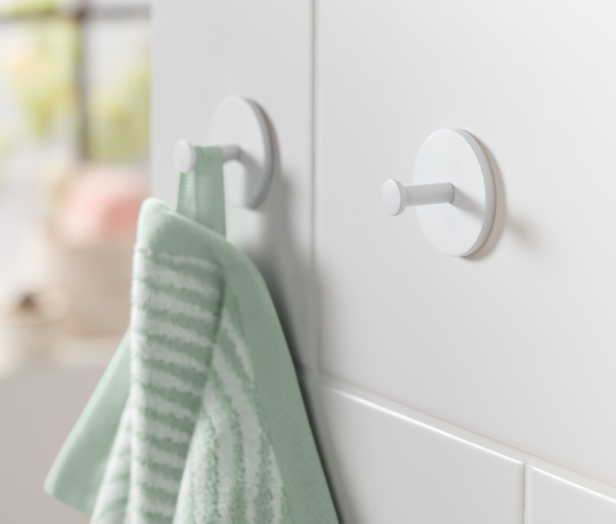 Ein grünes Handtuch hängt an einem von zwei weißen Haken an einer weißen Wand.