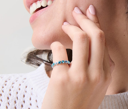 Lächelnde Frau berührt ihr Gesicht und trägt einen Ring Memory Blue Shades am Finger.