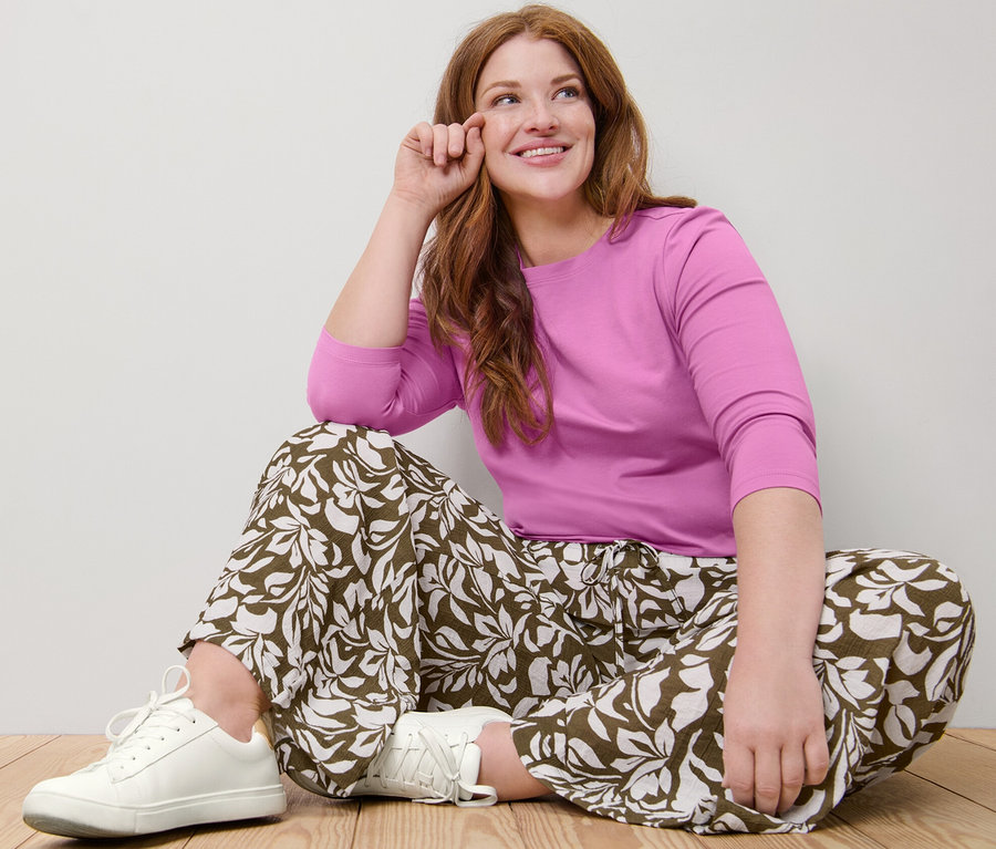 Frau sitzt auf dem Boden und trägt ein rosa Shirt mit 3/4-Arm und eine bedruckte Schlupfhose.