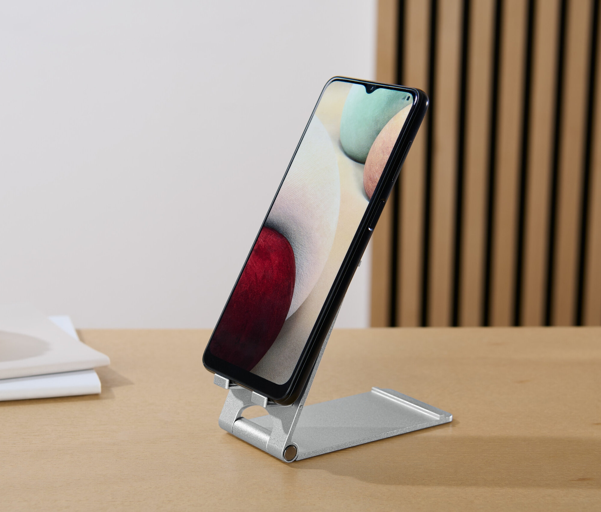 Ein schwarzes Smartphone steht auf einem Smartphone-und-Tablet-Ständer auf einem Tisch.